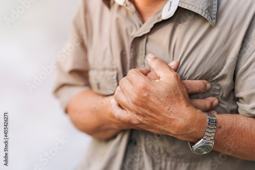Close-up of an elderly man's hand held his chest in pain. Concept of heart disease.