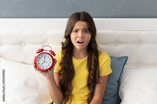 Worried girl child hold alarm clock being upset with oversleeping morning, late