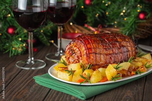 Baked veal roulade with potato and rosemary. Red wine glasses. Christmas holiday dinner on a dark wooden table with a Christmas tree and New Year's toys.