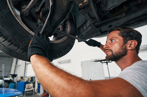 Man performing suspension system check using crowbar