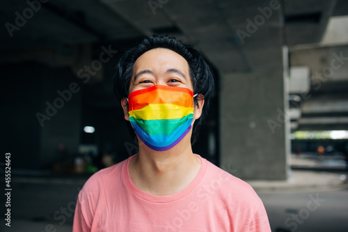 Young happy Asian man wearing a rainbow patterned mask representing LGBT support and pride during Covid-19 or Coronavirus