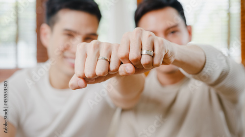 Portrait Young Asia Gay couple feeling happy showing ring at home. Asia LGBTQ+ men relax toothy smile looking to camera while hug in modern living room at house in the morning concept. Close up Shot.