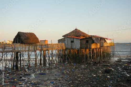 Obama Restaurant on stilts over the water, but a lot of dirty trash around at low tide. Evening, the last rays of the sun. Conakry, Guinea.