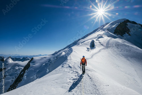 Before Mont Blanc (Monte Bianco) summit 4808m last ascending. Team roping up Man with climbing axe dressed high altitude mountaineering clothes with backpack walking by snowy slopes with blue sky.