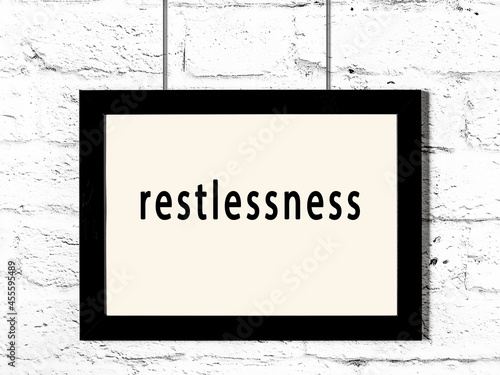 Black frame hanging on white brick wall with inscription restlessness