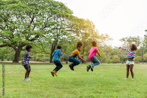 Group of African American children having fun jumping over the rope in the park. Cheerful kid jumping over the rope outdoor. Happy black people enjoying playing together on green grass