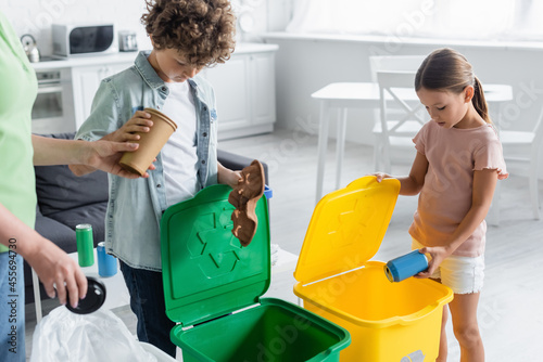 Kids sorting garbage near mother and trash cans with recycle sign at home