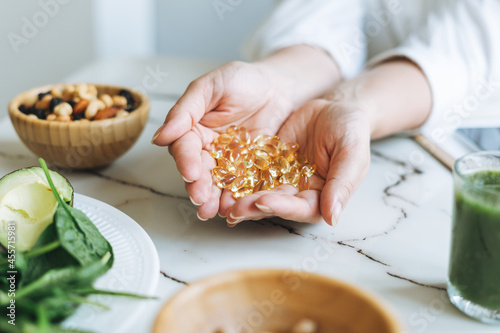 Woman doctor nutritionist hands in white shirt with omega 3, vitamin D capsules with green vegan food. The doctor prescribes a prescription for medicines and vitamins at the clinic