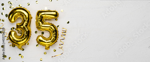 golden foil balloon number thirty five. Birthday or anniversary card with the inscription 35. gray concrete background.