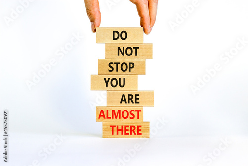 You are almost there symbol. Wooden blocks with words 'do not stop you are almost there'. Businessman hand. Beautiful white background, copy space. Business, motivation and almost there concept.