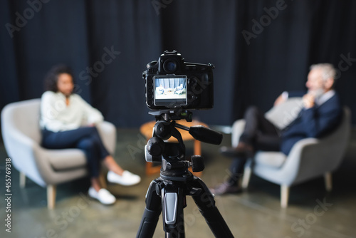digital camera with african american journalist talking with businessman during talk show on screen