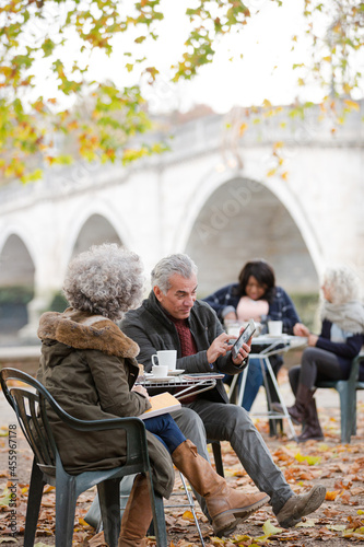 Senior couple using digital tablet, enjoying coffee and tea at autumn park