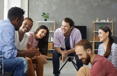 Young mixed race people having fun and enjoying good time together. Diverse group of six happy millennial friends sitting on the sofa in the living-room and laughing at a funny joke