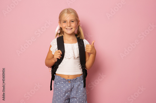 Little schoolgirl show thumb up isolated over pink background