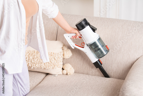 A woman is cleaning the sofa with a cordless vacuum cleaner. House cleaning.
