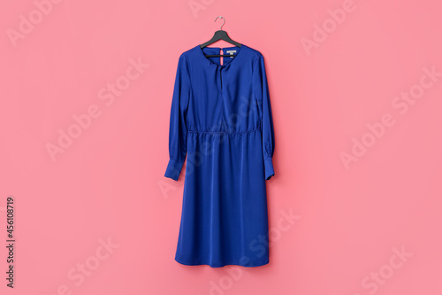 Hanger with stylish female dress on color background