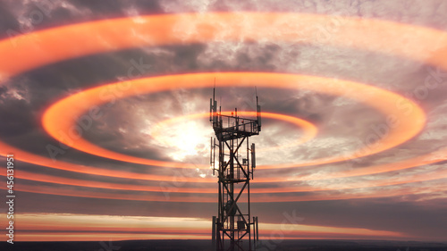 Wireless telecom radiation with aerial footage. Silhouette of telecommunication tower construction with antenna dishes on red sunset. Mobile digital radio waves animation from the high cellular mast.