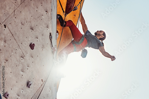Early morning workouts. One Caucasian man professional rock climber practicing alone at training center in sunny day, outdoors.