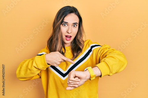 Young hispanic girl wearing casual clothes in hurry pointing to watch time, impatience, upset and angry for deadline delay