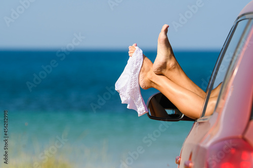 White swimsuit hangs on beautiful female legs from the car window on the background of the beach. The girl came to rest on a nudist beach. Nudist vacation concept
