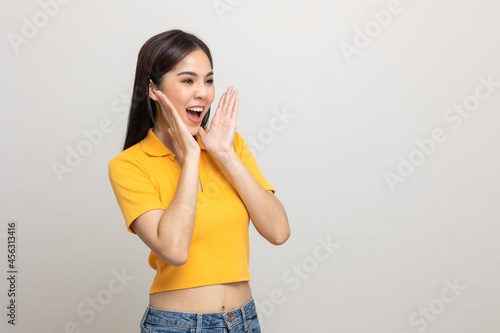 Excited asian woman shout out loud wow with hands on isolated background. Happy shocked face female wow promotion advertising concept. Joyful teenage girl in yellow shirt standing in white room.