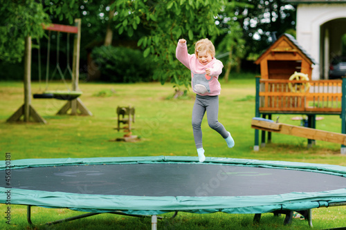 Little preschool girl jumping on trampoline. Happy funny toddler child having fun with outdoor activity in summer. Sports and exercises for children.