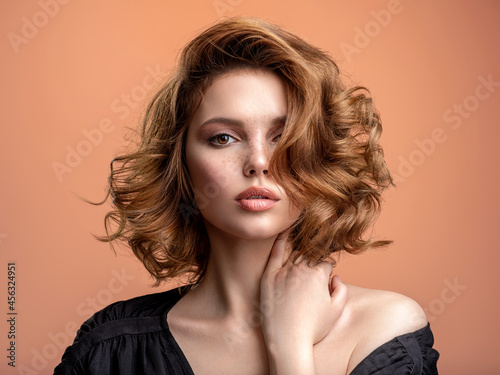 Beautiful brown haired with stylish short hairstyle. Woman with a curly hair. Beautiful young woman with freckles on face. Closeup portrait of an attractive girl with a brown makeup.