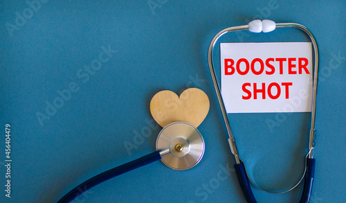 Covid-19 booster shot vaccine symbol. White card with words booster shot, beautiful blue background, wooden heart and stethoscope. Covid-19 booster shot vaccine concept.
