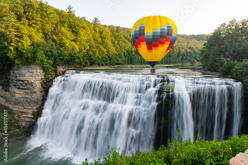 A hot air balloon flying low over the middle falls at Letchworth State Park in New York. The falls are shown in long exposure. 