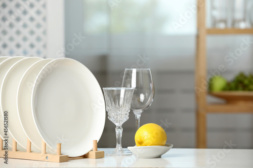 Clean plates in dish drying rack, glasses and lemon on white table indoors