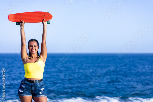 Young woman holding her skateboard on a blue sea background. Copy space. Lifestyle and sport concept