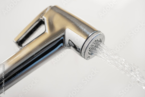 A chrome bidet shower spraying water, close up.