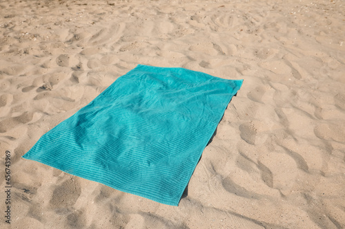 Turquoise soft beach towel on sunlit sand