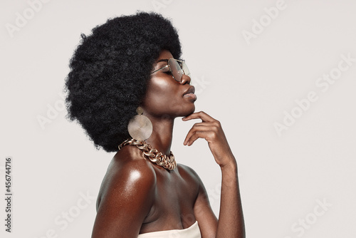 Side view of beautiful young African woman in golden jewelry keeping eyes closed and touching face