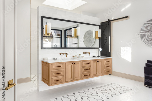 Bathroom in luxury home with double vanity. Features floating hardwood cabinets and faucets, large mirror, and elegant tile floor. A skylight allows for abundant natural light.