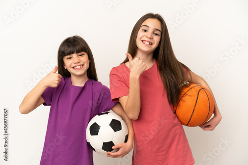 Little sisters playing football and basketball isolated on white background giving a thumbs up gesture with both hands and smiling