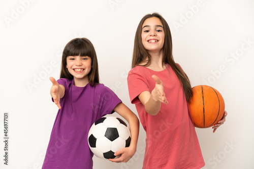 Little sisters playing football and basketball isolated on white background shaking hands for closing a good deal
