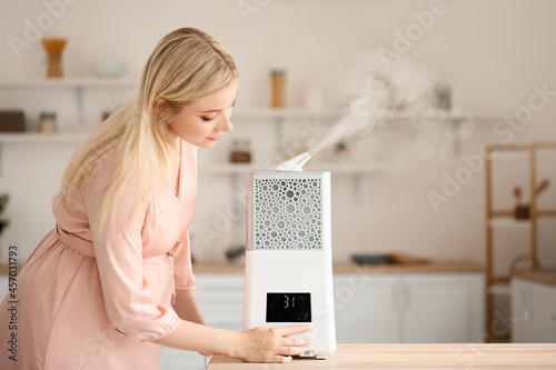 Pregnant woman with modern humidifier in kitchen