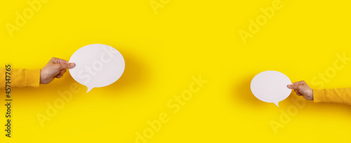 two talk bubbles speech icon in hand over yellow background, panoramic layout