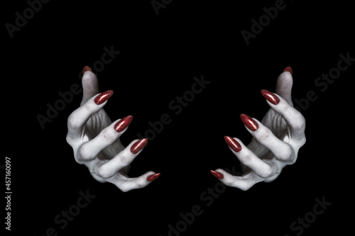 Bony pale hands of vampire or monster with sharp bloody red nails in the dark. Witch fingers hold something, low key, selected focus.