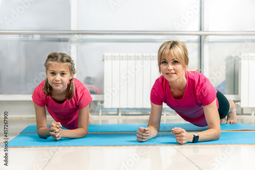Beautiful athletic woman and her daughter doing plank exercises on the floor in the fitness studio. Sports, fitness, healthy lifestyle together. Fitness Workout.