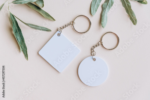 Keychain mockup among olive leaves to display design. Blank white sublimation key chain photo.