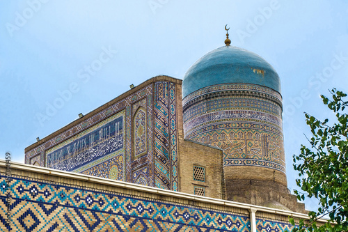 Dome, iwan and part of wall of Nadir Divan-Begi madrasa in Samarkand, Uzbekistan. Elements decorated with traditional patterns and ornaments. Inscriptions on building are quotes of suras from Koran