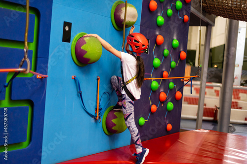 Girl wearing in harness and safety equipment climbing on practical wall indoor. Girl inserting the rope in a quickdraw.