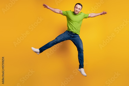 Portrait of funky dreamy positive cheerful guy jump raise hand on yellow wall