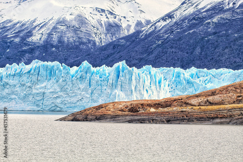 Vertical shot of glacier with rocky land and a mountain in the foreground