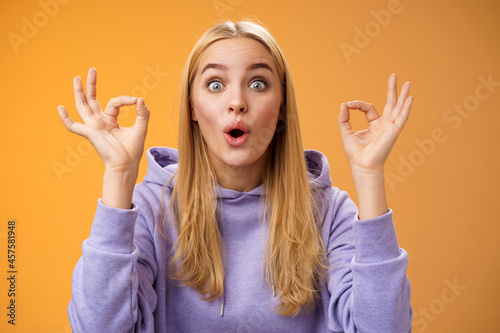 Amused talented creative young blond female tell excellent idea show okay no problem gesture persuade friends everything alright standing excited orange background ok signs, folding lips amazed