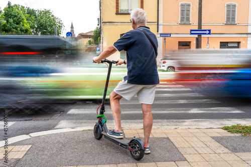 commuter hipster man using electric scooter is waiting to cross a road with heavy traffic