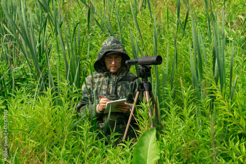 ornithologist records the results of the observations while standing among the tall grass in the wetland