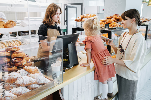 Mum with her daughter buying some pastry in a bakery shop.